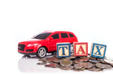 a red toy car next to a pile of coins with colourfull letter spelling out tax on top