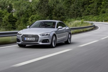 a metallic audi a5 coupe driving on winding tarmac road