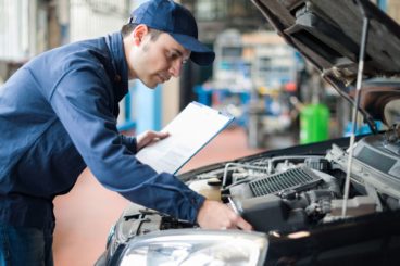 Man checking car engine with a clipboard