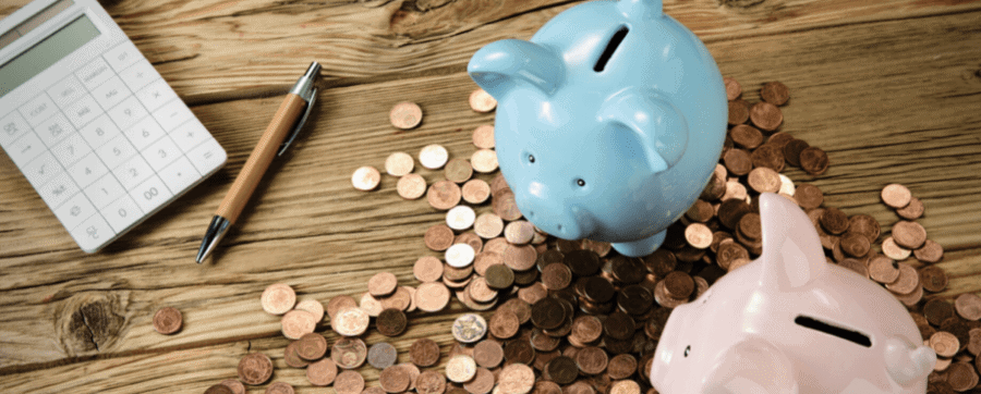 Piggy banks, coins, a calculator and a pencil laid out on a wooden table