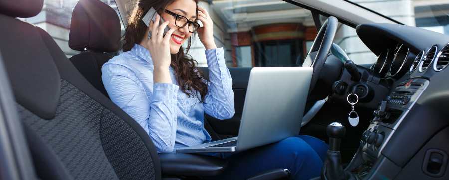 Is it worth having a company car - woman sitting in her car on a phone and laptop, working while the car is stationary