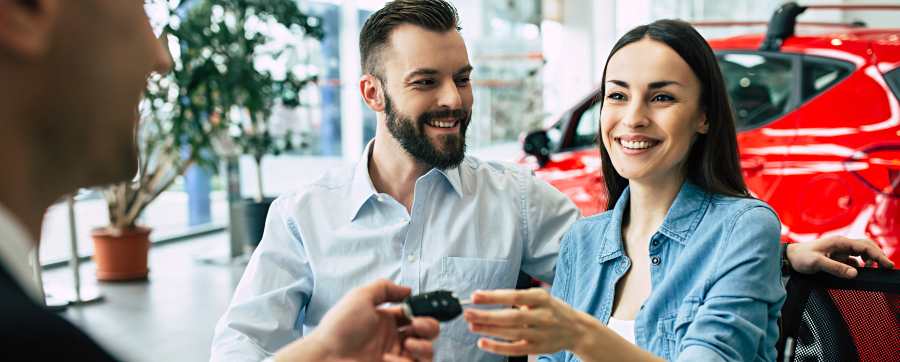 Car dealerships - couple in a car dealership receiving keys from a dealer