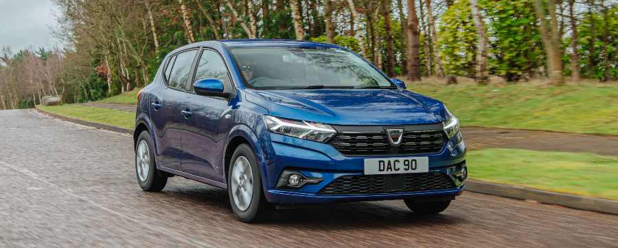 Blue Dacia Sandero car driving on a road surrounded by trees