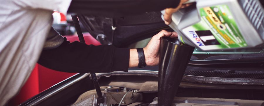 The front bonnet of a car is open, a person is filling the oil. They are holding a funnel and an oil container.