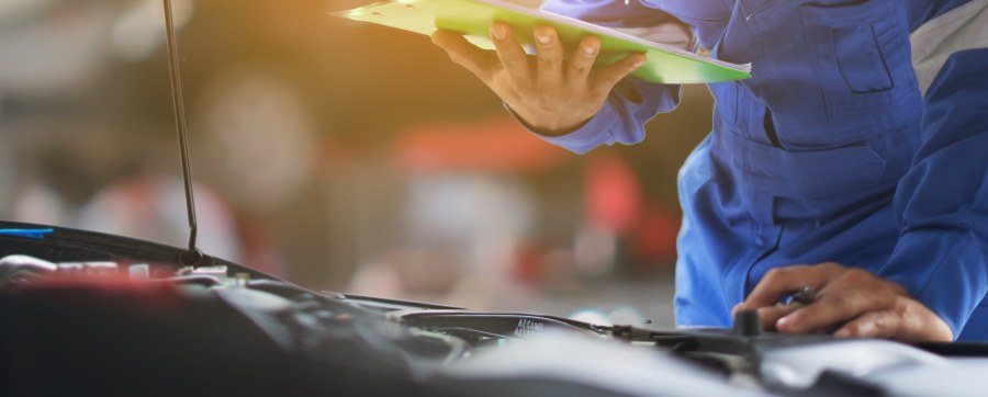 Mechanic standing besides a vehicle holding paperwork whilst working out how to fix the car