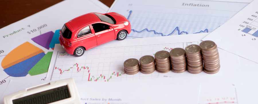 A small red toy car on top of finance papers, next to it are a stack of coins