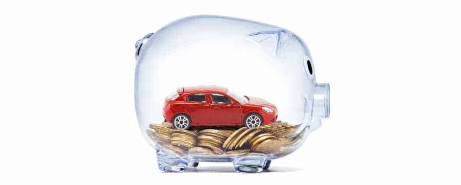 small red model car sitting on money coins in a glass piggy bank
