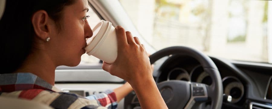 Female sitting in a car drinking a coffee whilst driving 
