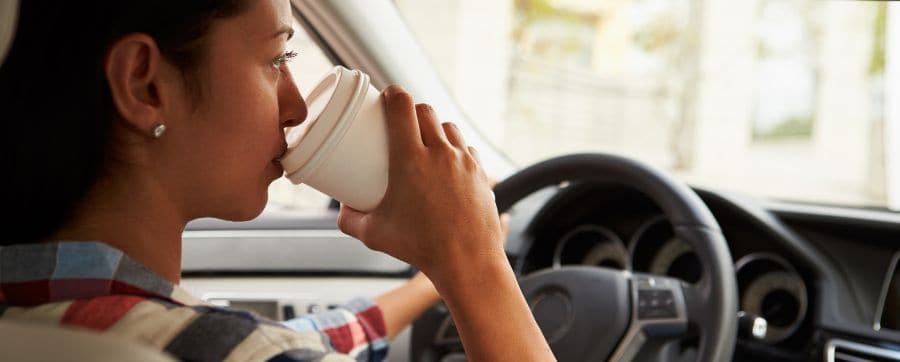 Female sitting in a car drinking a coffee whilst driving
