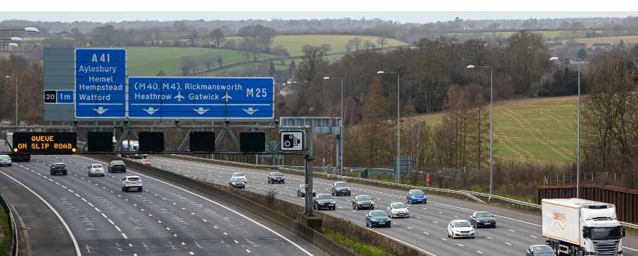 High view of an english motorway with the A41 M40 and M4 with vehicles driving on the road and a view of a field behind in the distance