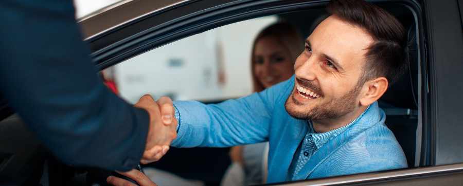 A man smiling in a car shaking hands with a dealer