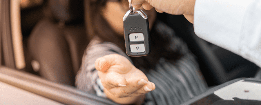 Hand holding a car key over another hand coming out of a car