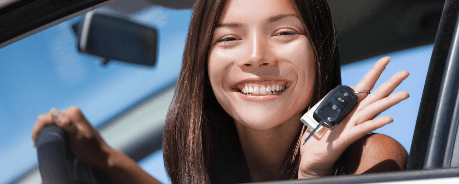 Woman smiling holding car keys whilst sat in a drivers seat in a new car