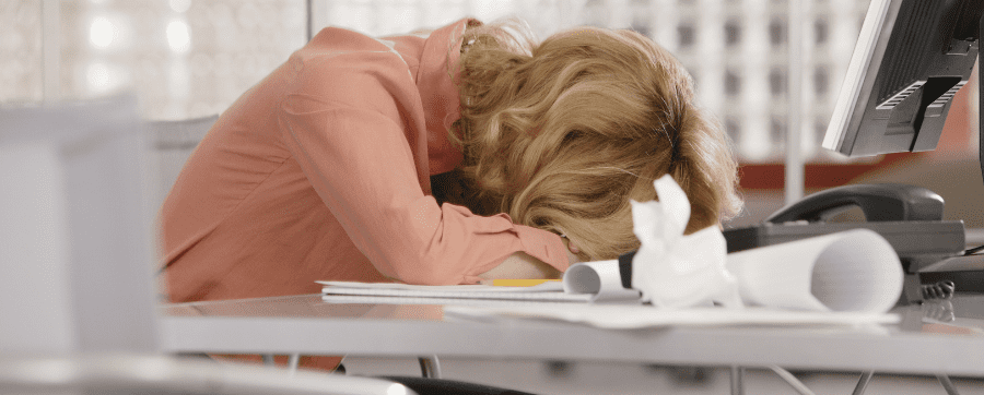 Working woman head down in stress on top of her desk with piles of papers and telephone