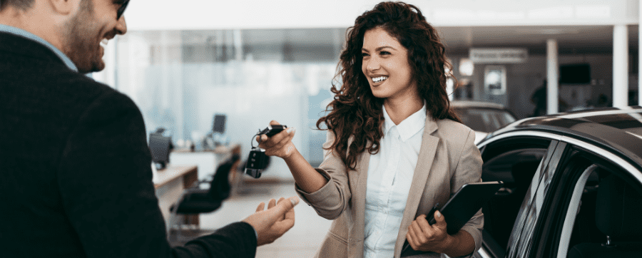 Sales woman smiling handing car keys to a man
