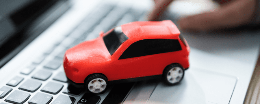 Small red car model resting on the keyboard of a grey laptop - car subscription UK