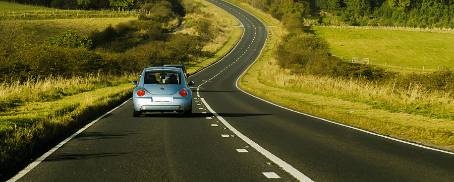 Blue car driving on a road surrounded by fields