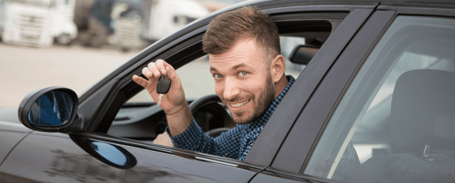 Man smiling holding car keys whilst sat in the drivers seat of a car