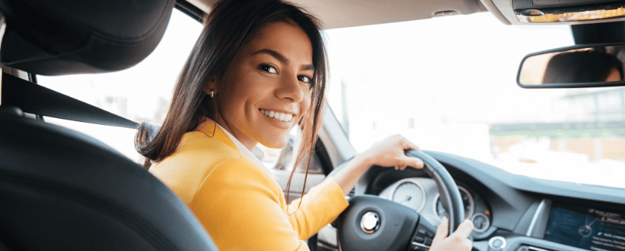 Woman in yellow jumper smiling sat in the drivers seat of a car - are car subscriptions worth it